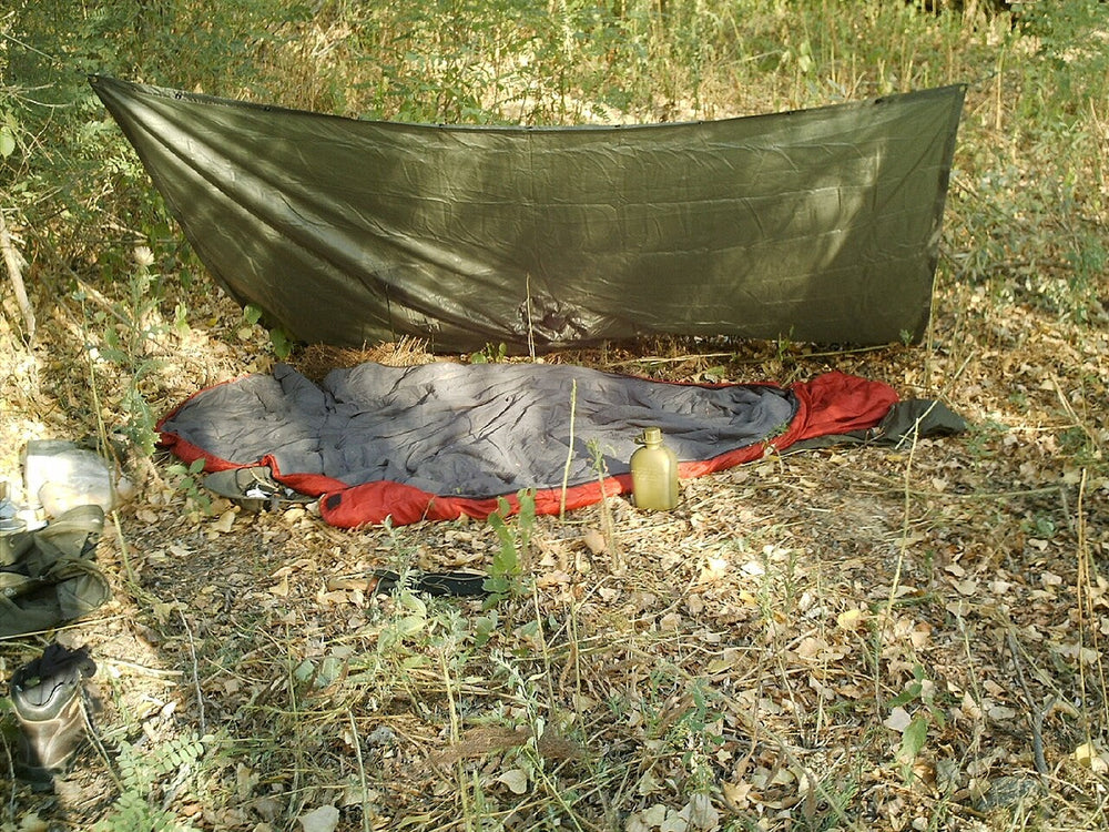 A poncho tarp pitched above a sleeping area outdoors.