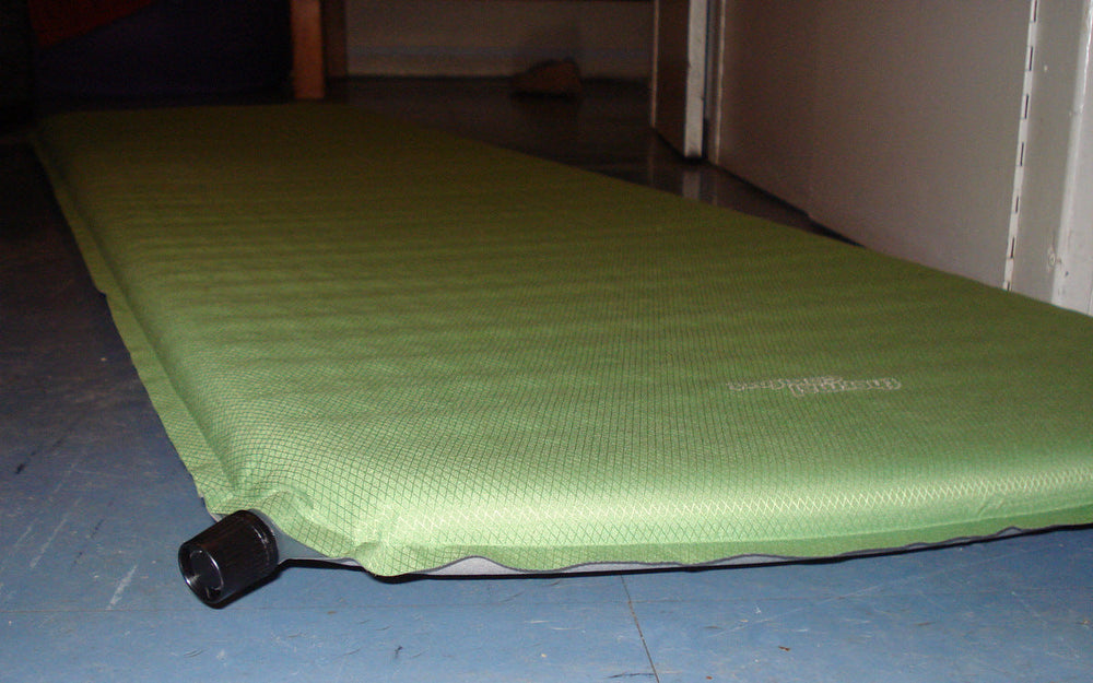 An inflated green self-inflating camping mat with its air valve visible.