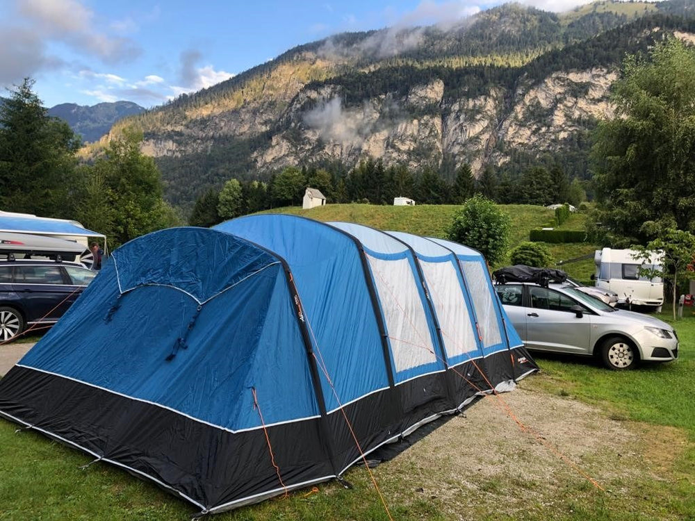 Blue family tent at a mountain campsite with cars behind it