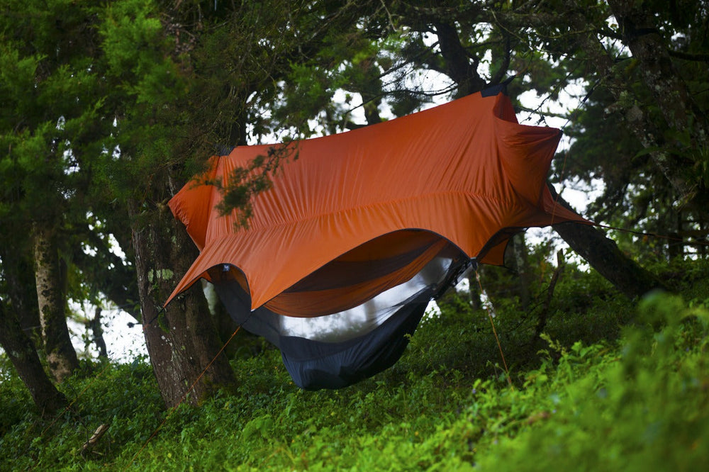 Camping hammock suspended beneath an orange rain tarp