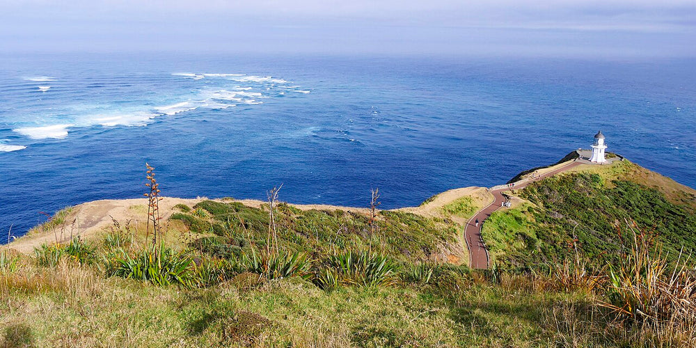 The paved headland path and lighthouse at Cape Reinga above the sea.