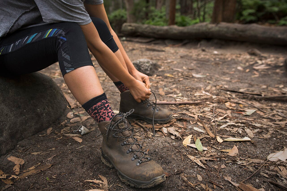 A walker wearing hiking socks while putting on brown boots.