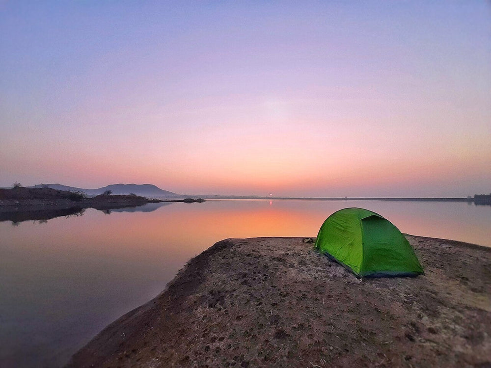Green camping tent beside water in cool morning light